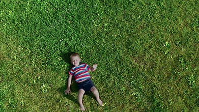 The cheerful boy lies on the green grass.