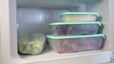 A man pulls frozen corn out of the fridge. Frozen fruits, vegetables, meat in the freezer.