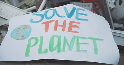 Close-up of Save the planet placard lying on trash. Concept of eco-activism and environmental pollution damage. Harmful
