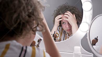 Teenage girl crushes acne while looking in the mirror.