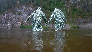 Funny flex in camouflage raincoats. Two teenagers perform synchronized dance moves in the rain, standing knee-deep in