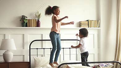 Happy little african kids boy and girl jumping on bed