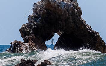 Sailboat seen through hole in arch rock
