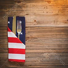 Fourth of July Table Place Setting with a fork, knife and flag napkin in warm light on rustic wood board background with room or s