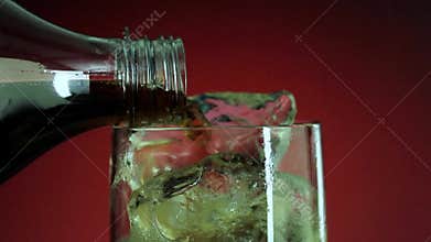 Pouring soft drink in glass with ice splash on red background. Cola or refreshment.