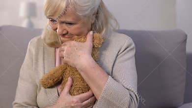 Lonely aged mother embracing teddy bear, remembering busy children, memories