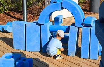 little boy is sitting on childrens playground in park with blue giant geometric figures for the development of imagination and