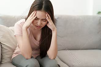 Asian woman are holding their hands to the head in pain on the sofa at home, Young women have severe headaches from migraines,