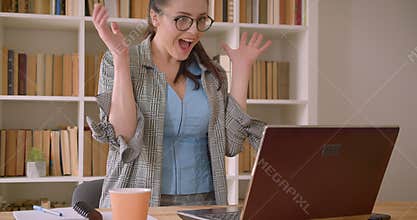 Closeup shoot of young successful caucasian businesswoman in glasses using the laptop and celebrating in the library