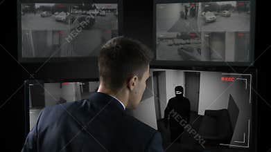 Security guard in front CCTV footage watching bank robbery, calling police