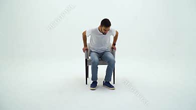 Handsome man in white tshirt and chair on a white background. Man gets up from the chair and going away.