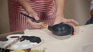 Ceramist girl is coloring by black paint clay bowl in studio of pottery