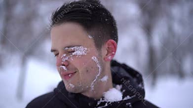 Close up of young caucasian man gets snowball on face during playing snowballs with friends, slow motion. Snowball fight