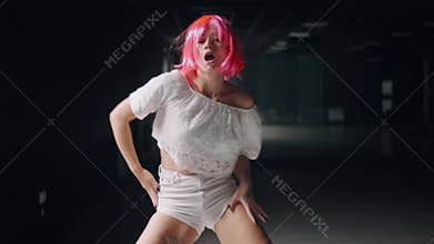 Hot girl is dancing at the dark studio background. Sexy pink woman is practicing dance