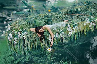 A brunette woman with long hair lies in a boat gently touches a water lily hand