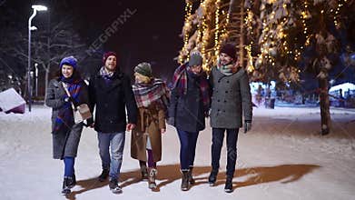 Group of happy friends walking under snowfall, have fun and communicate in slow motion. People hanging on snowy winter