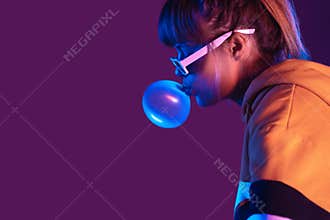 Teen girl wear stylish sunglasses hoodie blow bubble gum on purple background