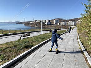 Vladivostok, Russia, October, 27, 2019. Boy roller skates along promenade in the bay of Patroclus Patrokl in autumn in clear wea