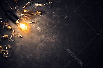 Vintage old light bulb glowing on rough dark background surrounded by burnt out bulbs. Idea, creativity concept