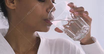 Thirsty african woman holding glass drinking water in morning, closeup
