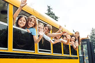 Classmates going to school by bus leaning out of the window waving to camera smiling positive