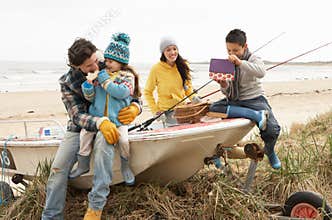 Family Sitting On Boat With Fishing Rod On Beach