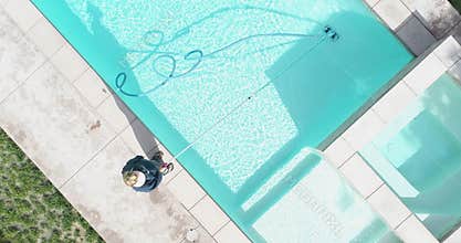 Overhead aerial of woman vacuuming swimming pool