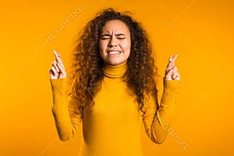 Cute curly young girl praying over yellow background. Woman begging someone.