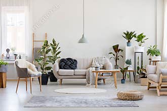 Urban jungle in trendy living room interior with white couch with black knot pillow and wooden furniture, copy space on empty wall