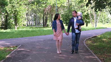Family portrait walking in city park with mom, dad and baby daughter in hands.