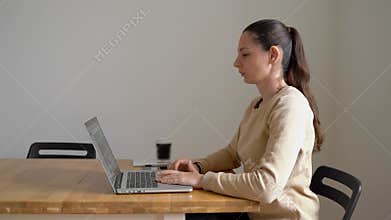Young woman sitting at the table and working on laptop with bad posture. Health problem. Scoliosis