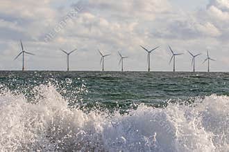Wind and wave energy. Breaking waves with offshore windfarm turbines background