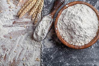 Wheat flour with scoop and wheat ears on kitchen board top view. Ingredient for baking