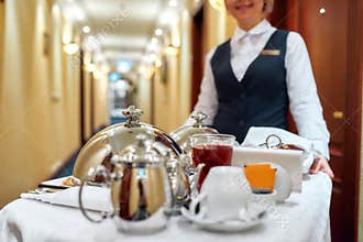 All that you need. Waitress in uniform delivering tray with food in a room of hotel. Room service. Focus on tableware