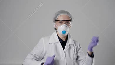 Cheerful female doctor is wearing protective mask, cap, glasses and gown is dancing in hospital, rejoicing