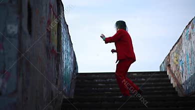 Cosplayer portrays a crazy clown  from the thriller `Joker` and dances on the stairs.