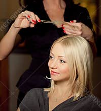 Haircutter cut hair in salon. Blonde woman