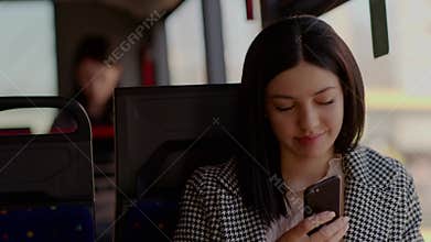 A young pretty girl sits in a public transport and chats cutely using her phone.
