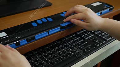 Close-up hands of person with blindness disability using computer keyboard and braille display or braille terminal a technology