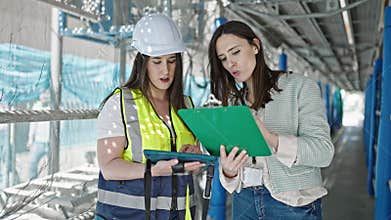 Two women architect and worker using touchpad writing on clipboard at street