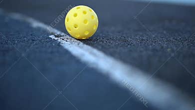 Perforated plastic ball for pickleball rolling on court in slow motion