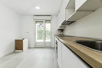 elongated kitchen with furniture on one side of the room, wooden countertop, white tiles with borders and cream-colored stoneware