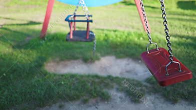 Children&#x27;s swings hang empty an idle at a playground on a dull.