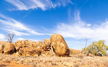 A jumble of granite boulders, blue sky with strange clouds and dry grass landscape
