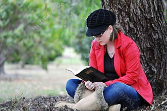 Pretty young girl reading holy bible under big tree in park