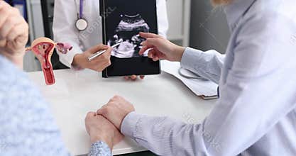 Obstetrician explains test results using tablet computer to caring husband and pregnant woman in clinic
