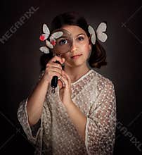 The girl looks through a magnifying glass. Butterflies sit on her head. Portrait in the old style.