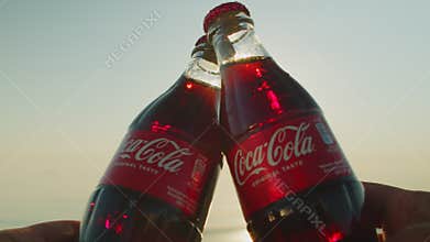 Friends checking glass bottles of Coca Cola beach against backdrop sunrise.