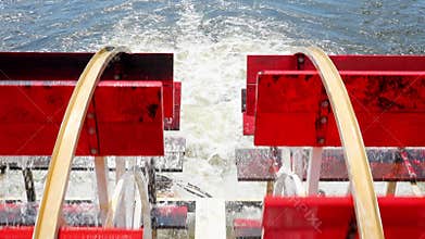 Closeup of red rotating paddle wheels of a cruise boat in motion.