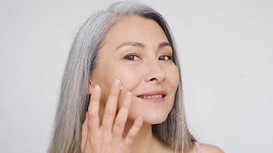 Happy mature asian woman looking at camera touching her face.